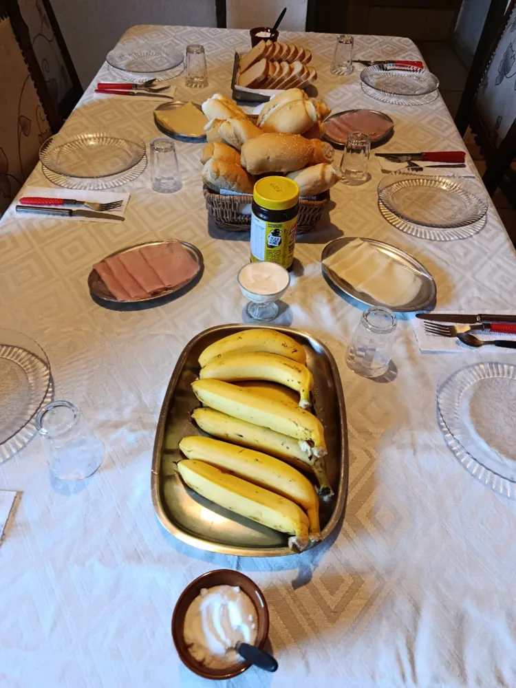Mesa de café da manhã posta com pães, frios, bananas e requeijão