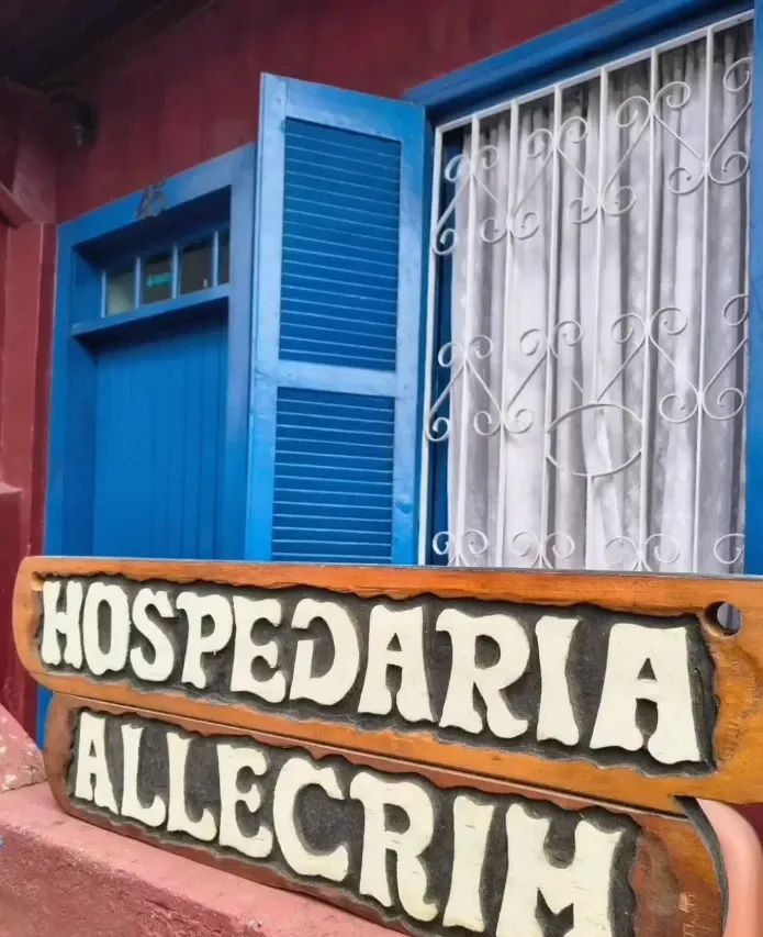 Fachada da Hospedaria Allecrim com a placa de madeira entalhada e janelas azuis